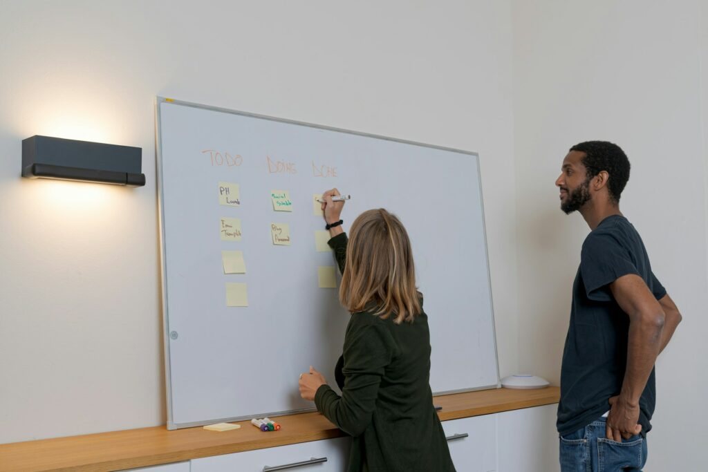 Make Black Friday Work for Your B2B Business 2 2. Two people collaborating and presenting ideas in front of a whiteboard covered with written content.