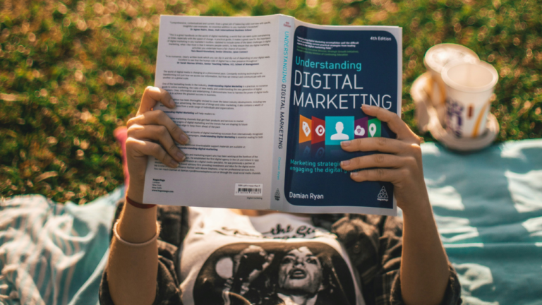 Insights 33 A person lies on a blanket in the grass, reading "Understanding Digital Marketing." A drink in a cup is beside them.